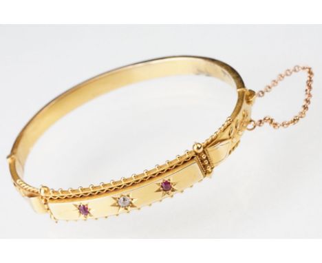 Edwardian diamond and ruby 15ct yellow gold hinged bangle, the central round old cut diamond weighing approx 0.15 carat, two 