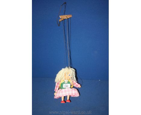 A wooden Puppet of a young girl in a pink check dress and a yellow rucksack.