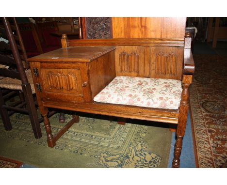 A Priory style medium Oak Telephone Seat with rear finial capped supports, twin linen fold carved back panel and scroll end s