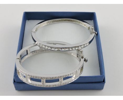 A Noemi rhodium-plated hinged bangle, set with Swarovski crystals; together with another similar. 