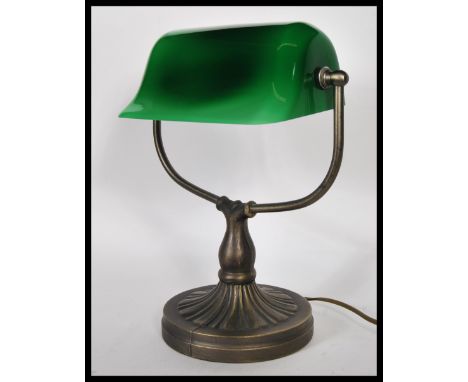 A vintage 20th century bankers desk lamp having an adjustable green glass shade raised on a brass support and good brass base