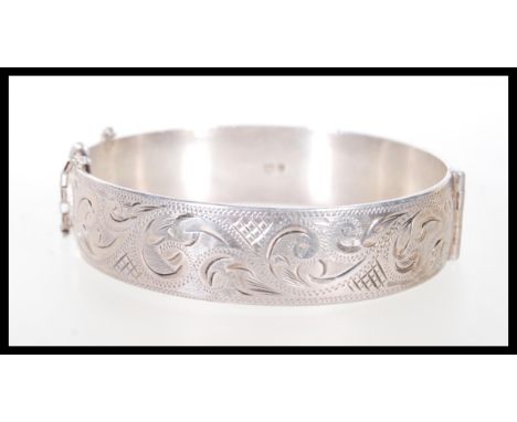 A hallmarked silver bangle with scrolled engraving and a hinge opening with safety chain. Hallmarked London 1962. Weight 47.8