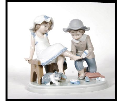A Lladro ceramic figure group titled ' Try this One ', (5361) of a young girl trying on a shoe. Stamped to base.