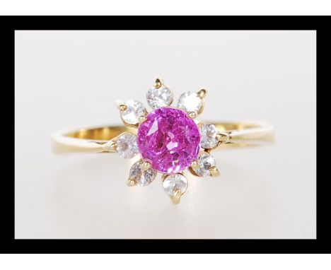 An unmarked 18ct gold ladies dress ring prong set with a round cut pink stone with a halo of white accent stones. Unmarked bu