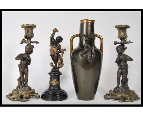 A 20th Century garniture of mantelpiece ornaments to include a pair of cast metal figural candlesticks being raised on scroll