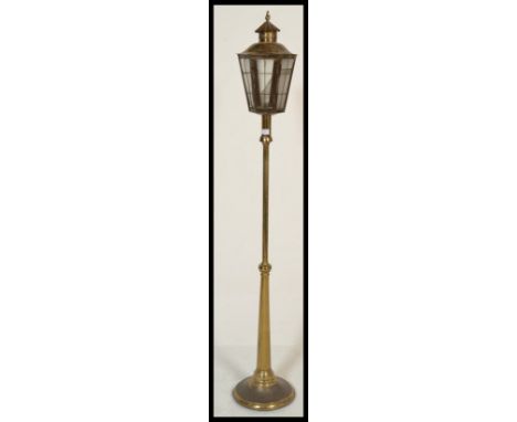 An Arts &amp; Crafts style brass standard lamp in the form of a street lantern, the square glazed tapered hood enclosed by a 