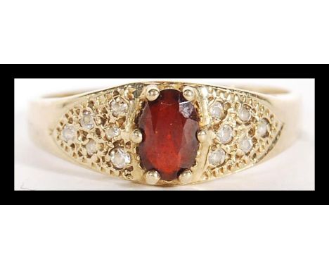 A 9ct gold diamond and garnet hallmarked London ring. Oval garnet adorned with diamond chip accented shoulders. Total weight 