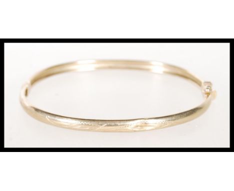 A stamped 375 9ct gold bangle bracelet with engraved decoration having a hinge opening. Weight 6.6g. Measures 2 1/2 inches wi