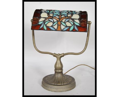 A good 20th century brass bankers desk lamp raised on a round base with a leaded and stained glass shade having a floral desi