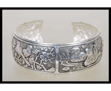A Chinese silver bangle having panels of repousse decoration of animals including mandarin ducks, deer, peacock etc. Unmarked