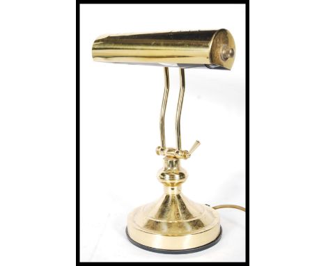 An Antique 20th Century style brass effect bankers lamp, having tubular shade and adjustable stem, raised on a circular stepp