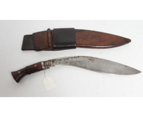 A MILITARY KUKRI, the 13 1/4" blade of typical form stamped with broadarrow, two piece wood grip and leather scabbard bearing