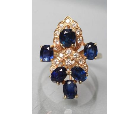 A SAPPHIRE AND DIAMOND DRESS RING, the six oval facet cut sapphires claw set with small diamond pave set borders to a plain s