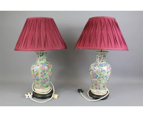 Two Porcelain Base Lamps. The lamps having a floral design with burgundy pleated shades and set on&nbsp;wooden bases, approx 