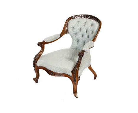 A Victorian carved walnut framed upholstered button back open armchair. Having an openwork crest over a waisted backrest, ext