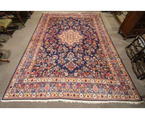 A large blue ground rug. The dark ground decorated with a dense pattern of blue, red and orange leaves, echoed in the beige a