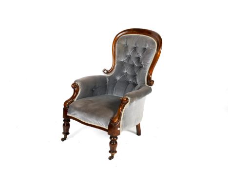 A Victorian mahogany framed button back armchair. Having carved scroll arms, raised on turned supports with casters, upholste