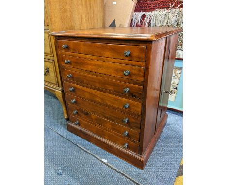 A late 20th century mahogany collectors cabinet with a leather inset top over seven drawers, locked by a side panel on a plin