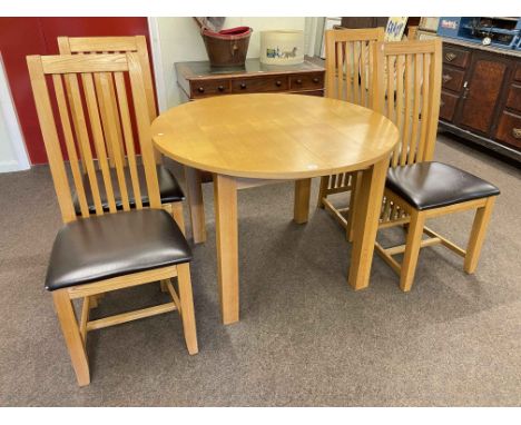 Circular light oak extending dining table with integral leaf and four rail back dining chairs.