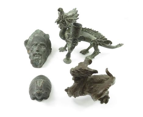 A metal candlestick in the form of a dragon; a metal wall hanging sculpture of a man wearing a feathered cap; and two other m