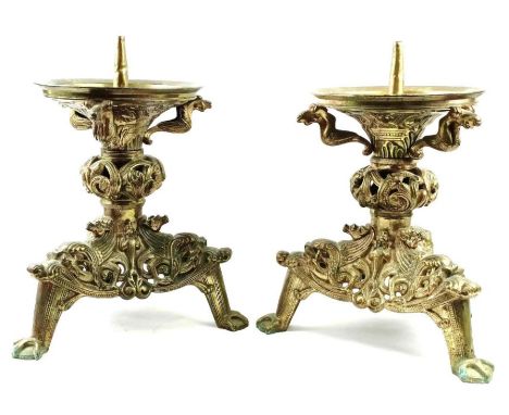 A pair of 19th century brass church candlesticks, heavily decorated throughout with animals and motifs, standing on a tripod 