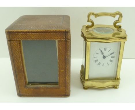 A 19TH CENTURY SERPENTINE BRASS CASED CARRIAGE CLOCK having white enamel dial with Roman numerals, 12cm high, in outer protec