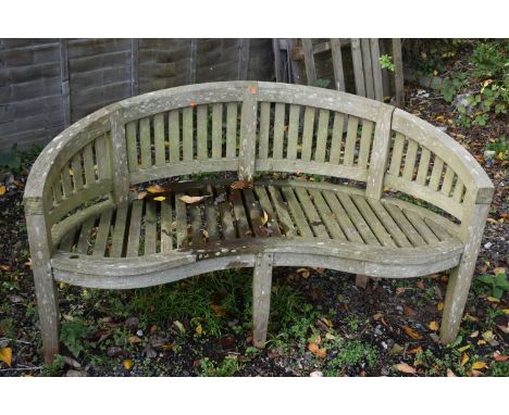 A WEATHERED TEAK CURVED BANANA BENCH, length 151cm (condition report: left art rickety)