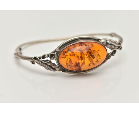 A SILVER AMBER BANGLE, designed as an oval cabochon of heated amber within a collet mount to the bifurcated shoulders featuri