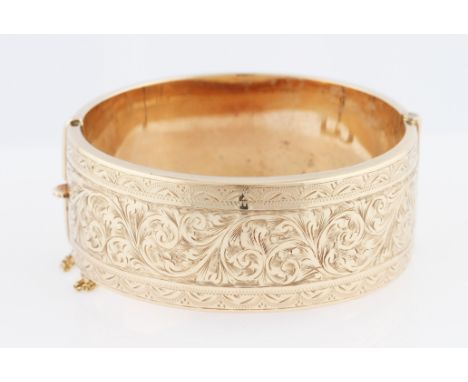 A 9ct yellow gold hinged bangle, half engraved with scroll design, width approx. 2.5cm, weight approx. 37.6g.
