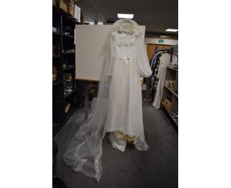 A vintage 1960/70s cream wedding dress with bell sleeves size 15' across chest with a veil and headdress sold along with a si