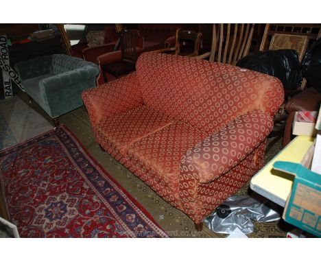 An Edwardian two seater Sofa with scroll end arms, upholstered in red ground fabric with circular motif pattern, standing on 