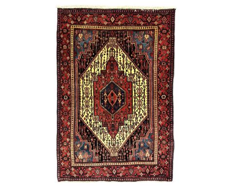 Northwest Persian Senneh crimson ground rug, central ivory lozenge medallion with geometric motifs, framed by matching spandr