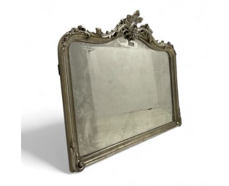 Overmantle mirror in silver finish frame, the swept frame decorated with curling foliage and flower head motifs, plain mirror