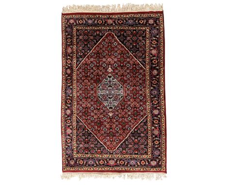 Persian crimson ground rug, central light blue lozenge medallion with floral motifs, the densely decorated crimson field fill