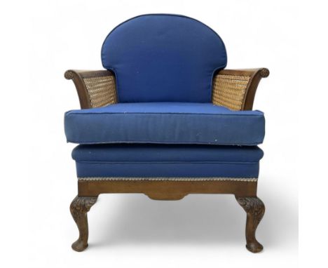 Early 20th century walnut framed bergère armchair, cane sides and back, upholstered in blue fabric, on acanthus carved cabrio