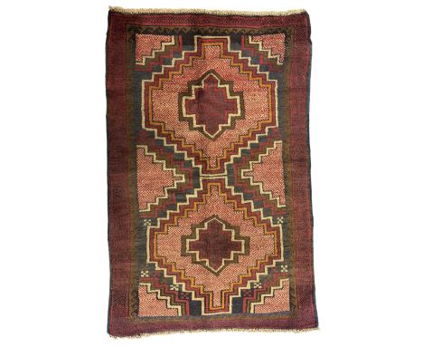 Baluchi crimson ground rug, the central field decorated with two stacked geometric lozenge medallions, surrounded by stepped 