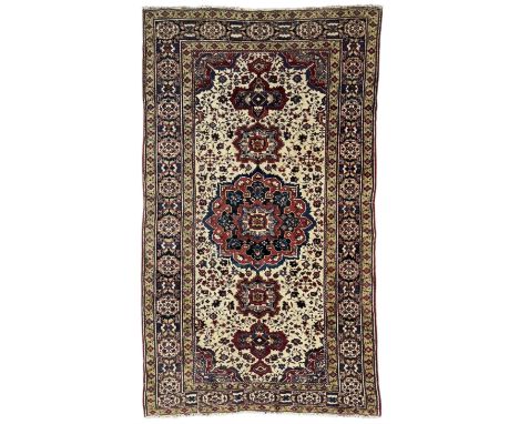 Persian ivory ground rug, central medallions in crimson, navy, and gold tones, surrounded by a floral field, framed by navy b