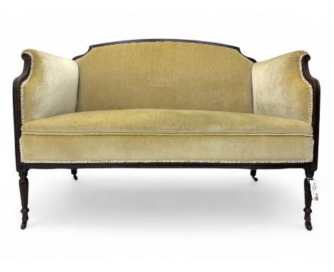 Early 20th century mahogany framed two seat sofa, upholstered in fawn fabric with braid trim, on turned reeded supports with 