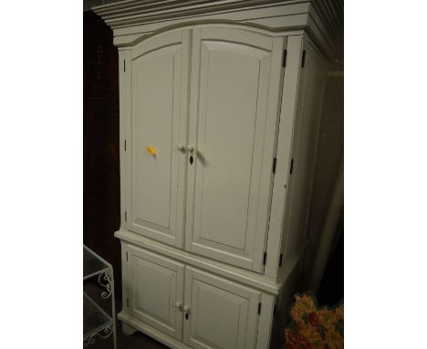 An American style white painted cupboard with flared cornice, two arched panelled doors enclosing shelves and drawers, fitted