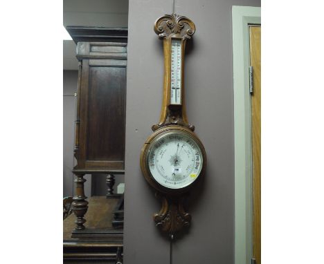 An aneroid barometer and thermometer in ornately carved and stained oak banjo pattern mount.