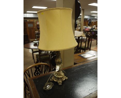 A modern ornate cast brass table lamp with mustard coloured shade.