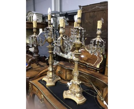 A pair of neoclassical gilded metal and resin moulded three branch table lamps, with foliate cast sconce and faceted glass dr