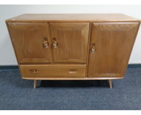 An Ercol elm and beech three door sideboard on raised legs (as found) CONDITION REPORT: Damages to handles. 