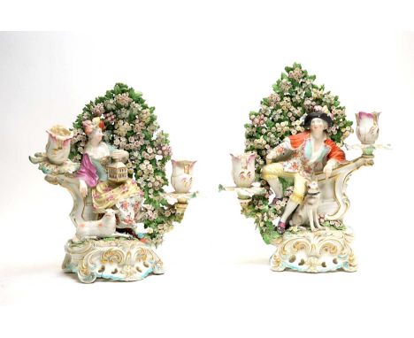 A pair of Derby candlestick figures of a shepherd and shepherdess, circa 1770. The shepherdess depicted with a lamb and birdc