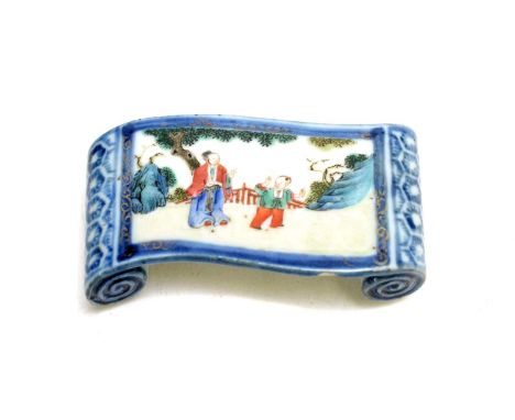 A Chinese famille verte brush stand, probably Kangxi, of scroll form, decorated with a woman an boy in a fenced garden, under