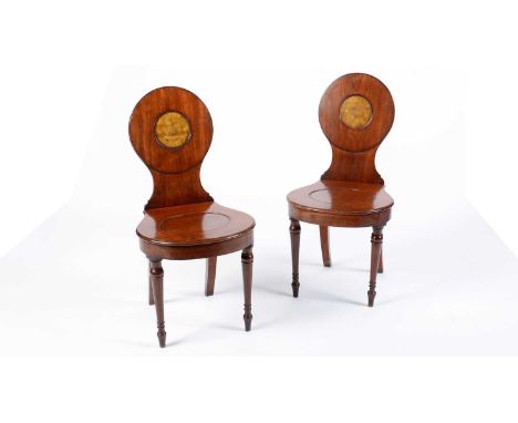 A pair of early 19th Century mahogany hall chairs, the circular backrests each with inset satinwood panel, over a panelled se