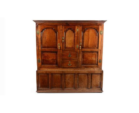 A large 18th Century oak clothes press/livery cupboard, the flared pediment above a narrow central panel door opening to reve