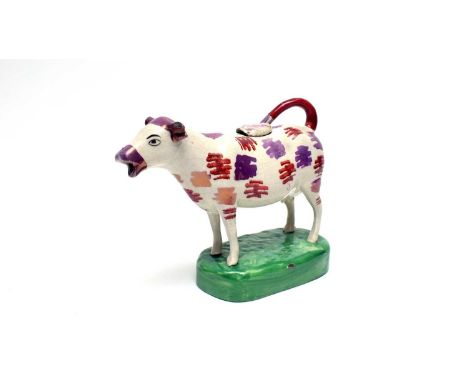 A lustre pottery cow creamer and cover, probably Cambrian, with iron-red and pink lustre decoration, on a green mound base, 1