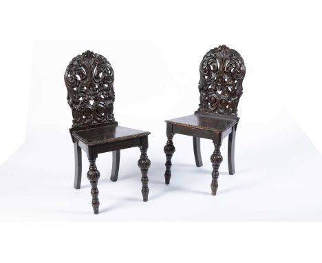 A pair of 19th Century carved oak hall chairs, the highly decorative backrests with foliate and floral detailing, over a pane