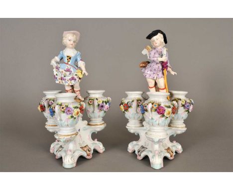 A pair of German porcelain table centrepieces, probably Dresden modelled as male and female winged figures in bright polychro